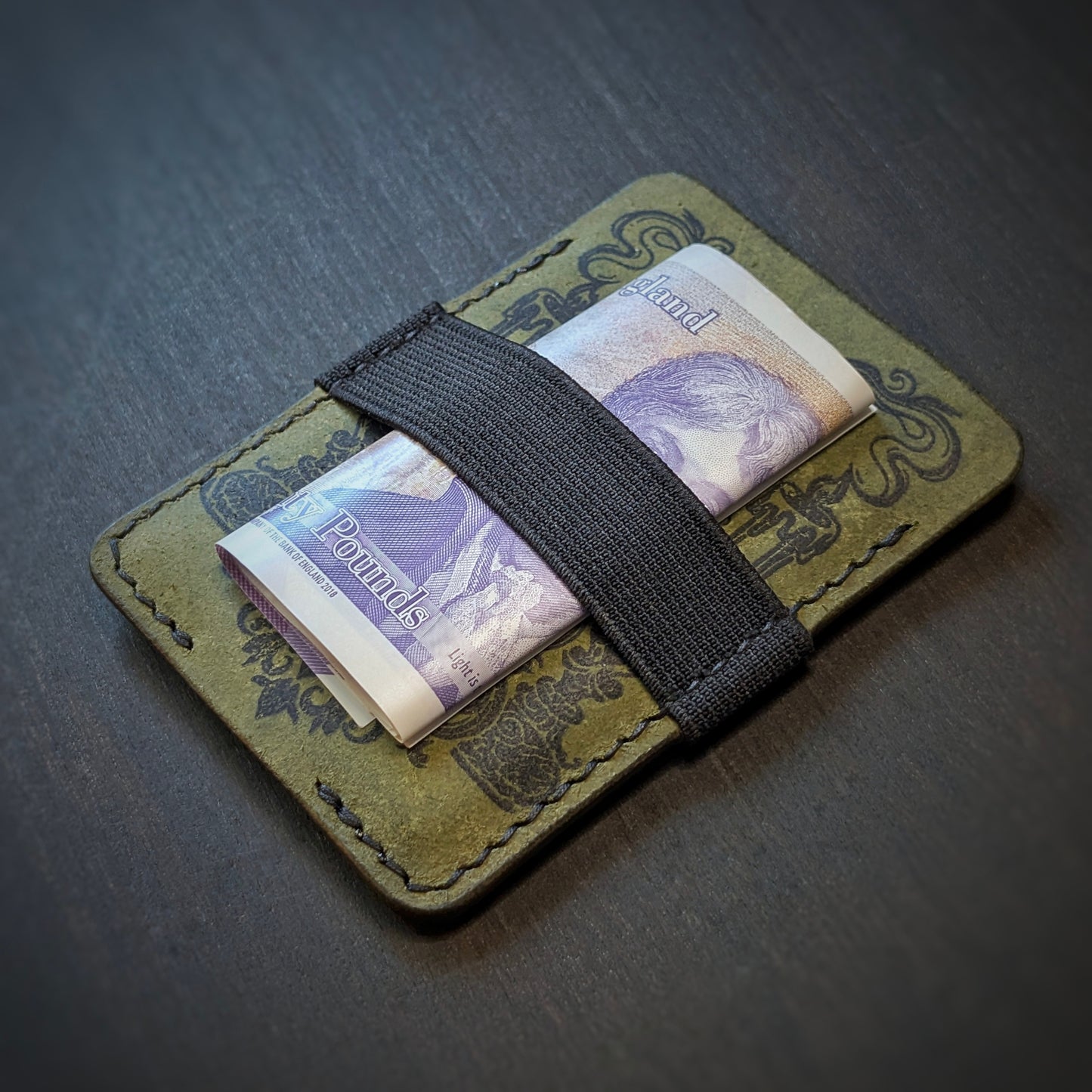 Olive Melee EDC wallet by El Rey Leather holding a folded UK banknote under a black elastic strap.