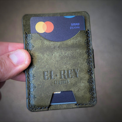 A close-up of a hand holding the El Rey Leather Melee minimalist wallet in Olive, showing the stamped details.