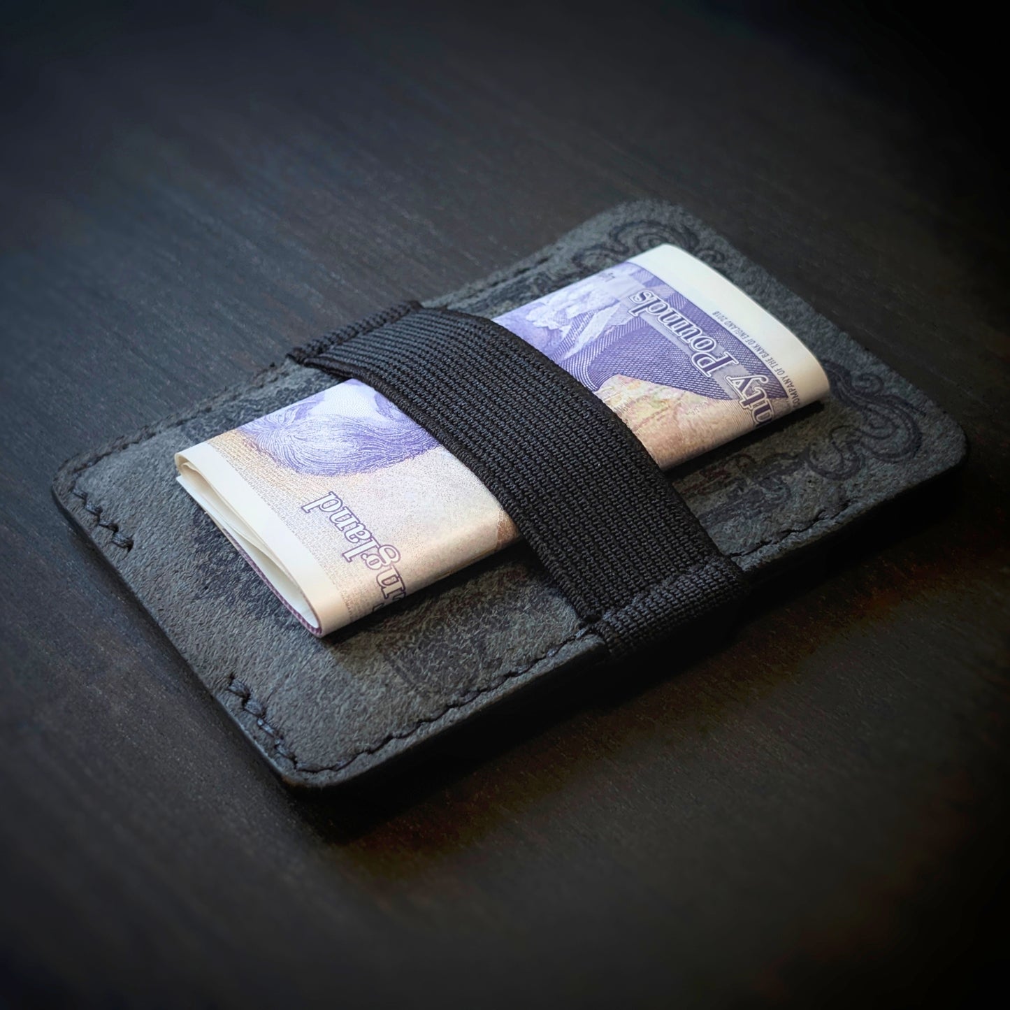 Black Melee EDC wallet by El Rey Leather holding a folded UK banknote under a black elastic strap.