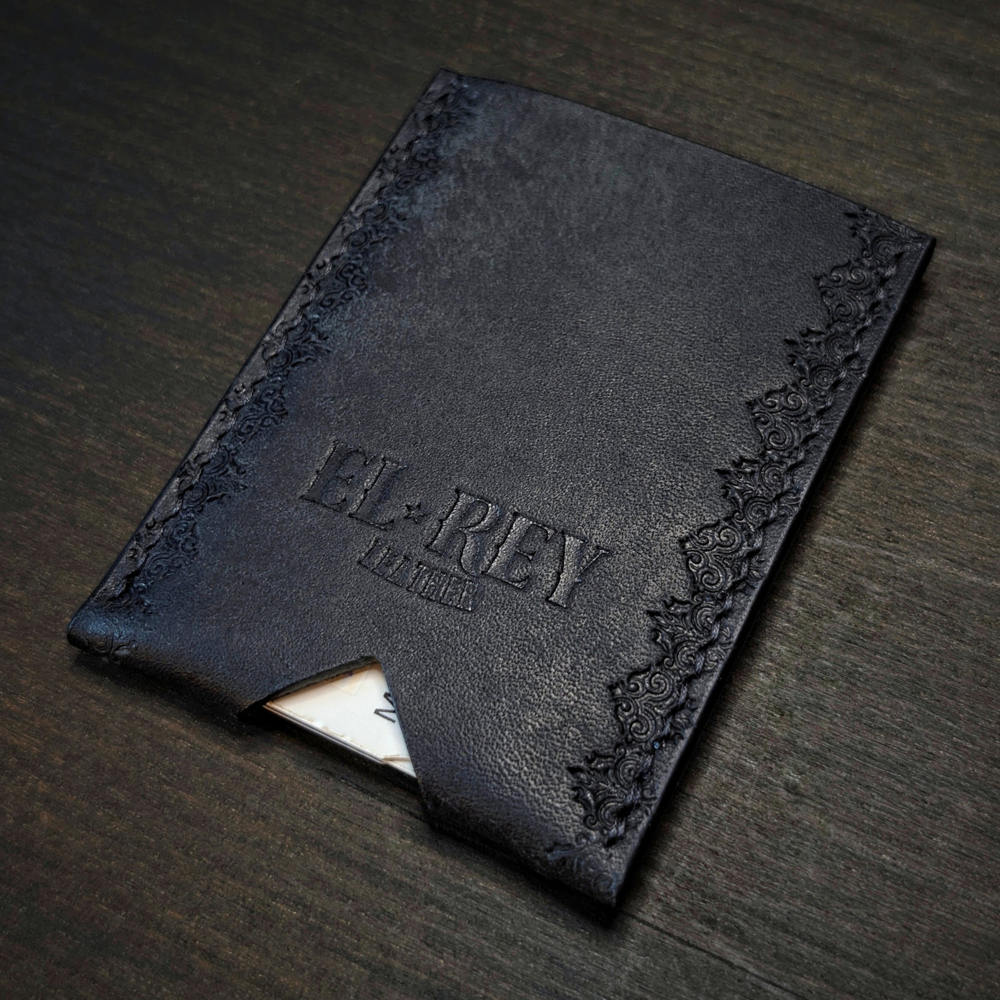 Rear angled view of El Rey Leather's Deadbeat minimalist wallet in black with cards, showing the hand-stamped border.