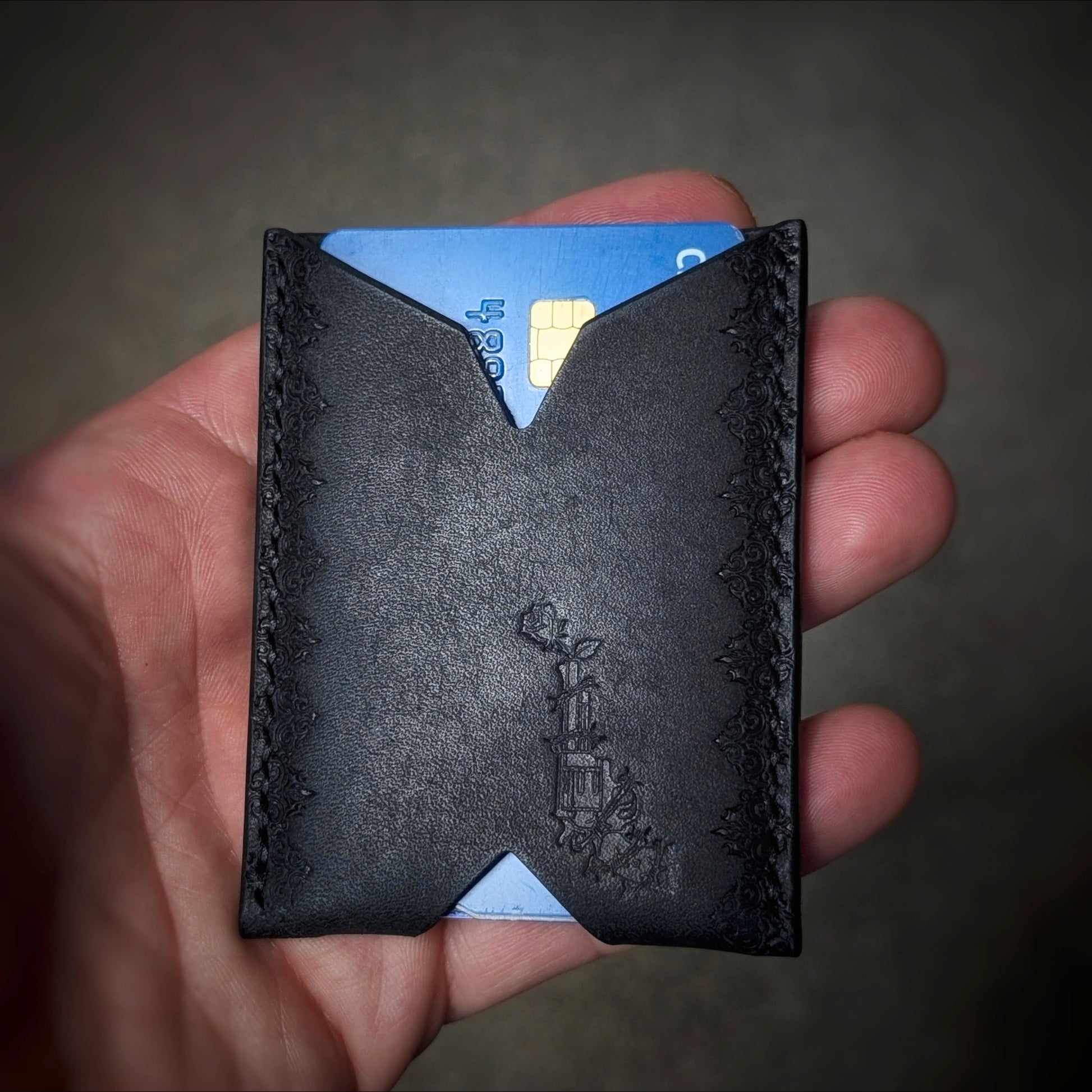 A close-up of a hand holding the El Rey Leather Deadbeat minimalist wallet in black, showing the stamped details.