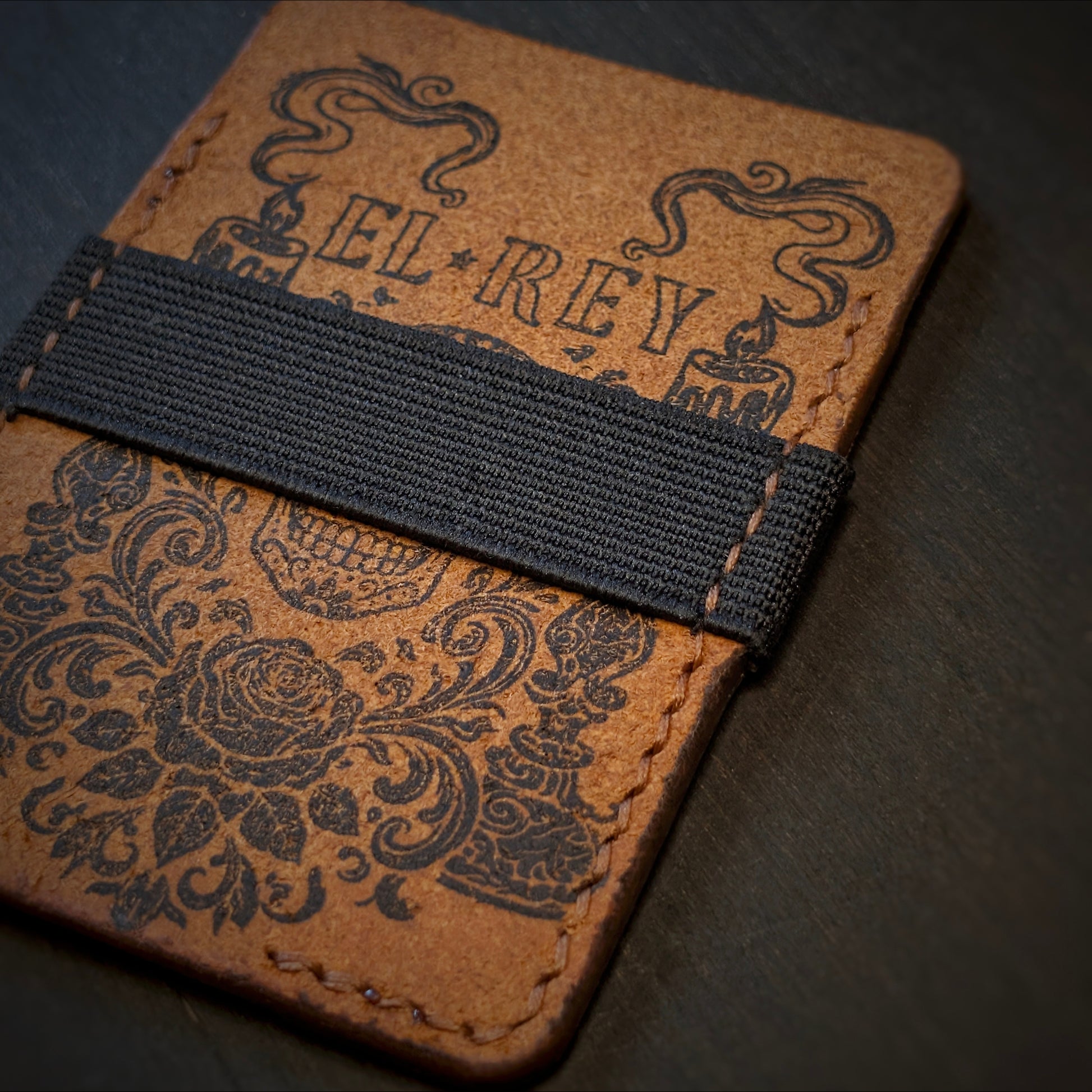 Close shot of the authentic El Rey Leather elastic cash strap and ink design on the Cognac Melee wallet.