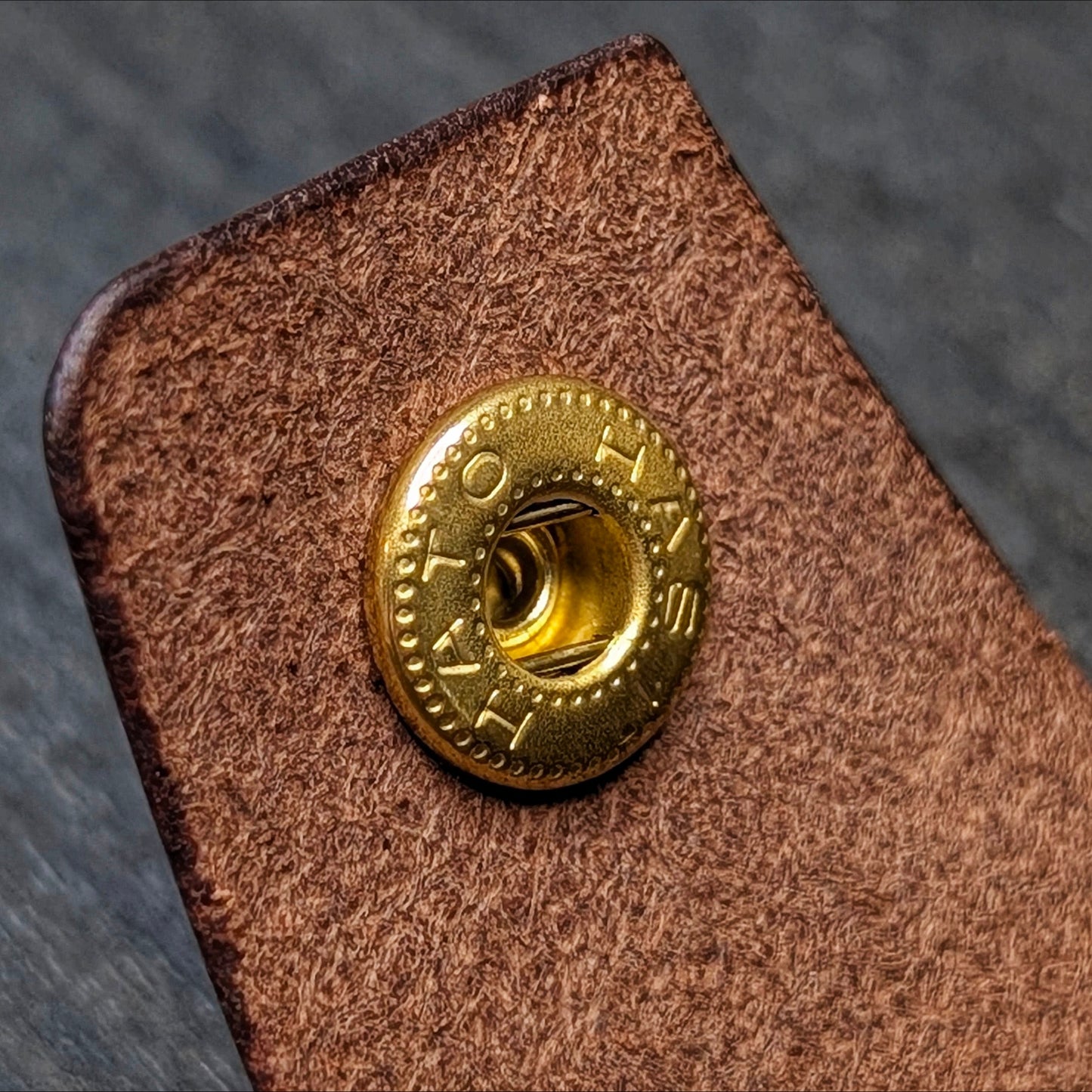 Macro texture shot of the strap and brass snap button on the handcrafted tobacco Lowlife everyday carry wallet.