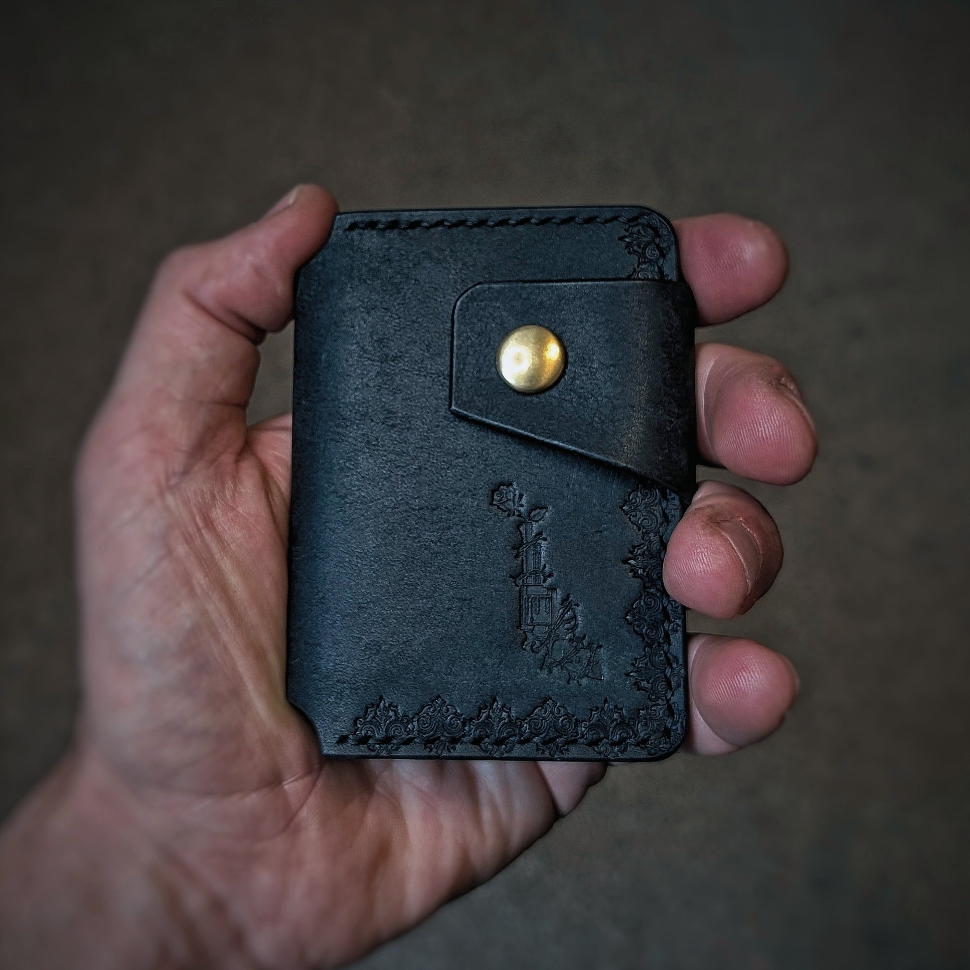 A close-up of a hand holding the El Rey Leather Lowlife minimalist wallet in black, showing the stamped details.