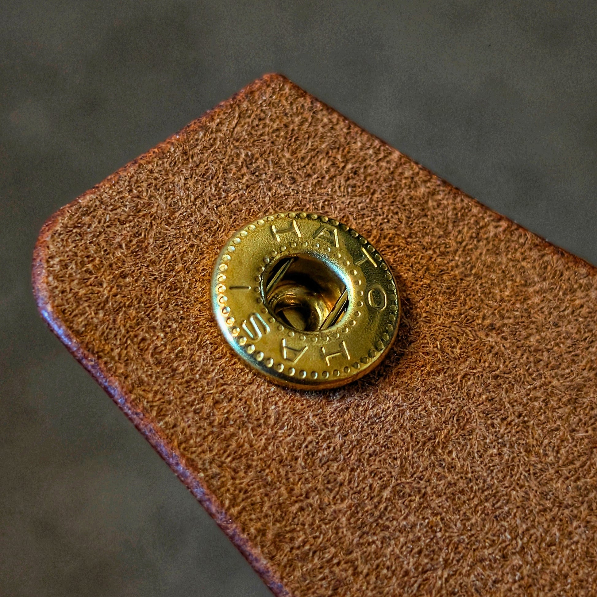 Macro texture shot of the strap and brass snap button on the handcrafted cognac Lowlife everyday carry wallet.