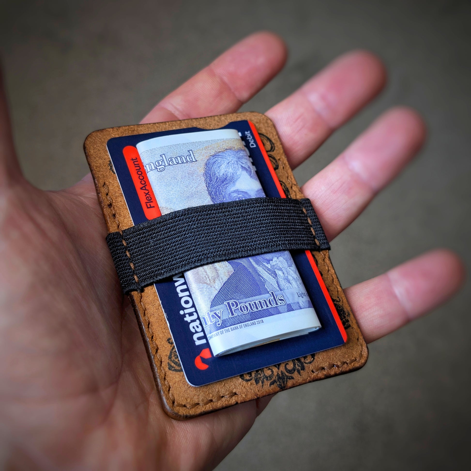 An open hand holding the El Rey Leather Melee EDC wallet in Cognac to demonstrate the woven elastic strap.