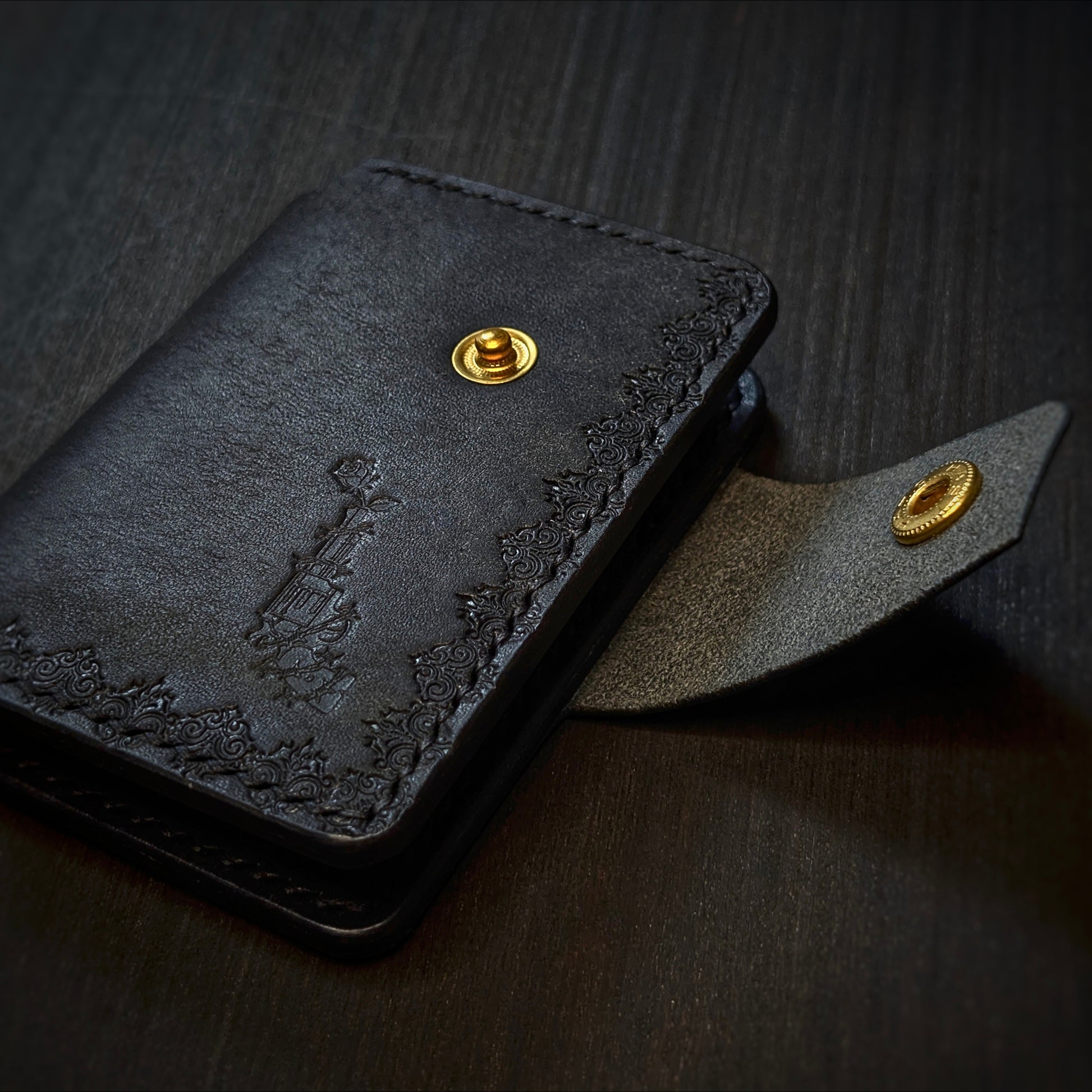 Angled view of El Rey Leather's Lowlife minimalist wallet in black, showing the strap and brass snap button..