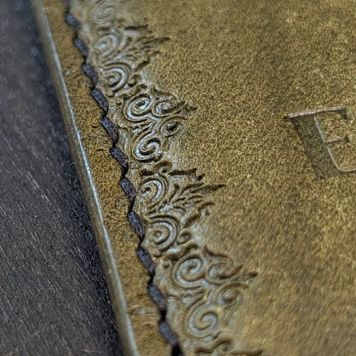 Macro shot of saddle stitching and gothic border stamp design on The Deadbeat olive leather wallet.