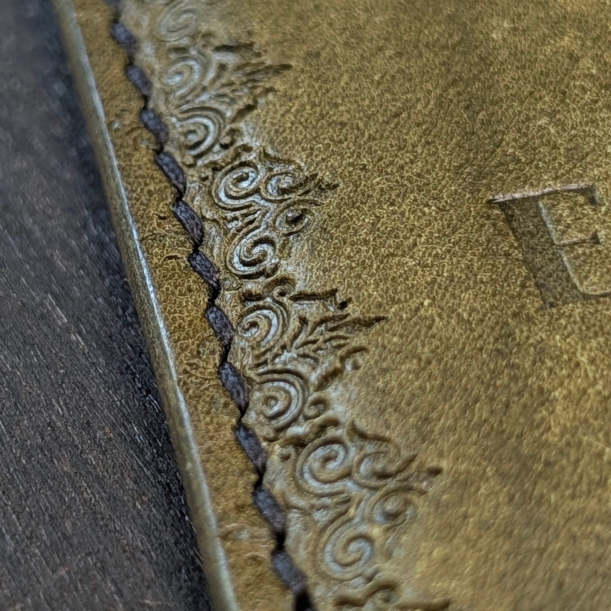 Macro shot of saddle stitching and gothic border stamp design on The Deadbeat olive leather wallet.