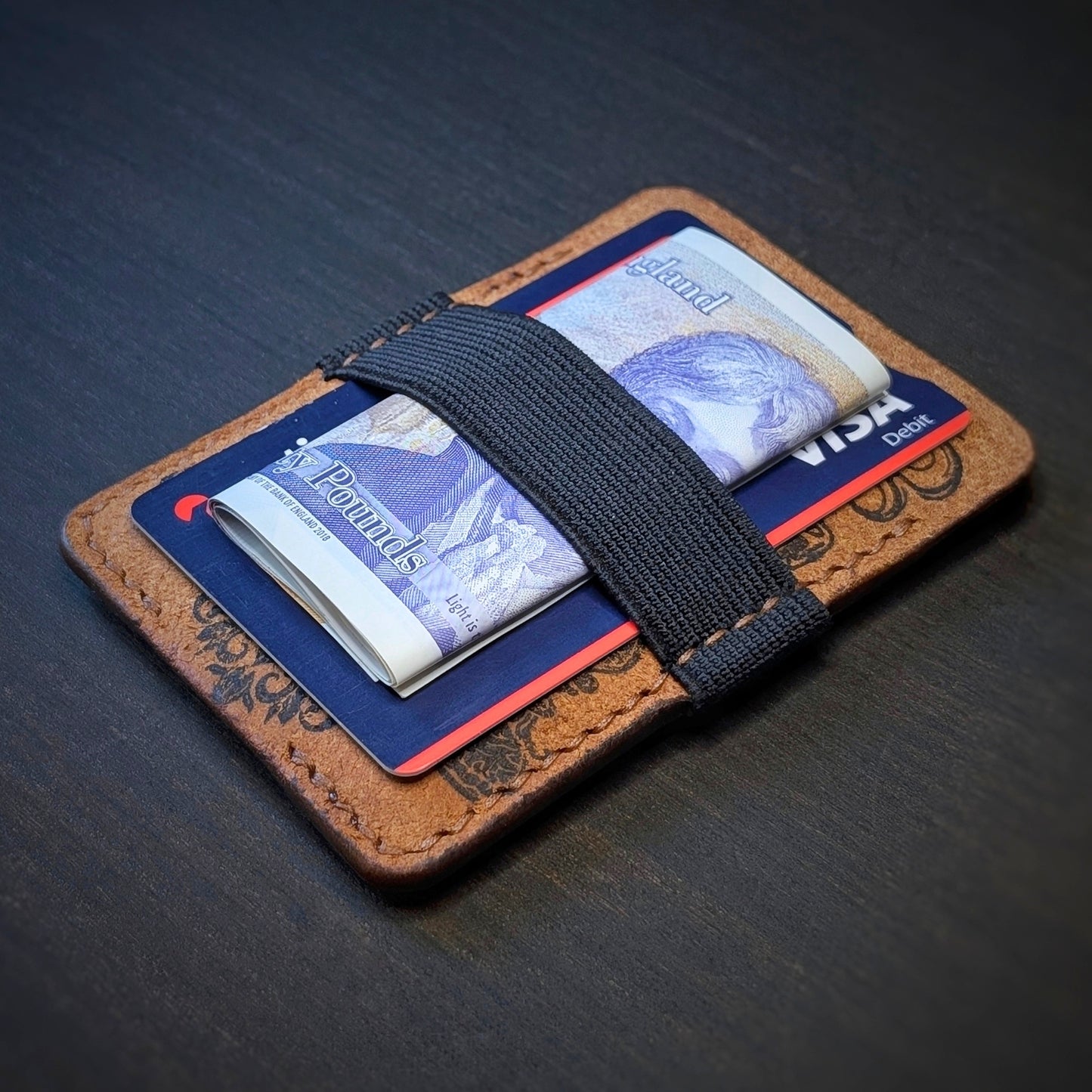 Cognac Melee EDC wallet by El Rey Leather holding a folded UK banknote and credit card under a black elastic strap.
