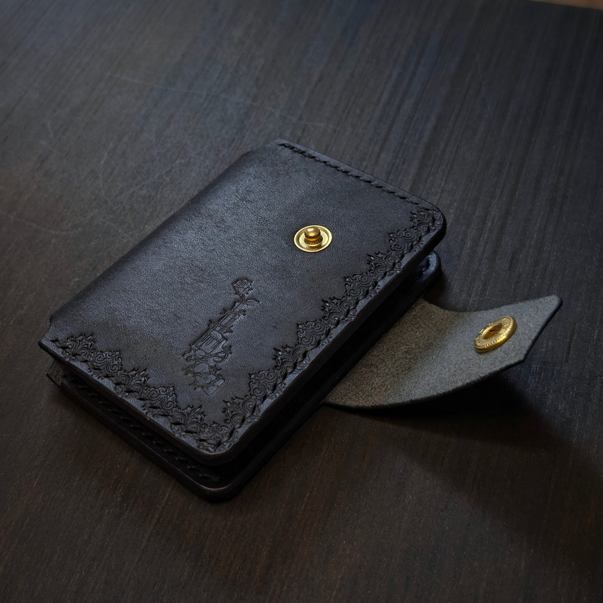 Angled view of El Rey Leather's Lowlife minimalist wallet in black, showing the strap and brass snap button.