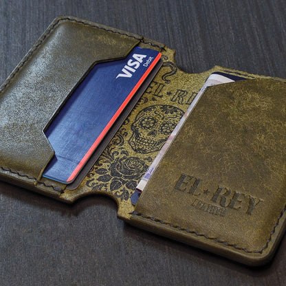Angled view of El Rey Leather's Lowlife minimalist wallet in olive with cards, showing the ink skull and embossed logo.