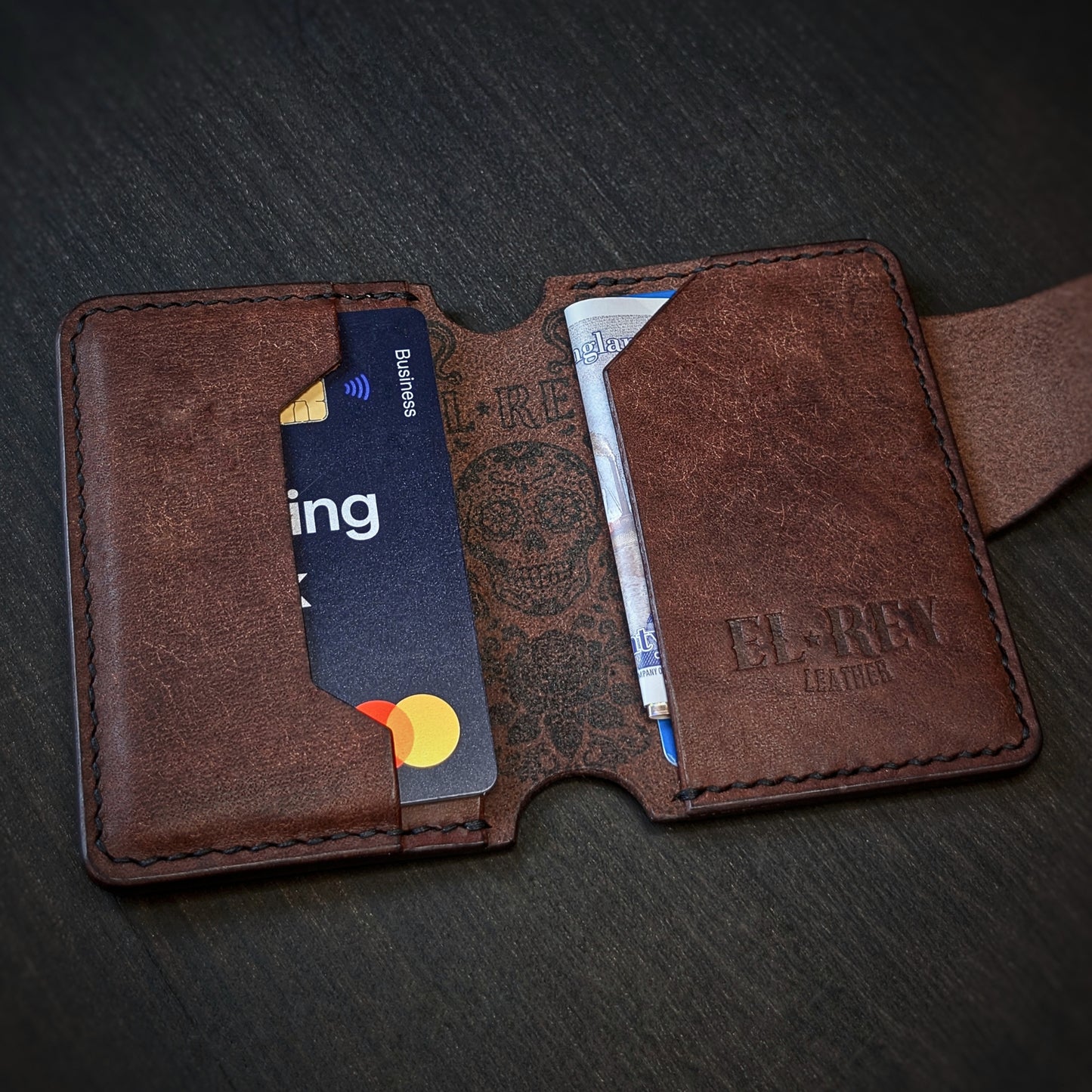 Angled view of El Rey Leather's Lowlife minimalist wallet in tobacco with cards, showing the ink skull and embossed logo.