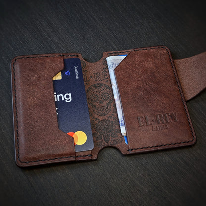 Angled view of El Rey Leather's Lowlife minimalist wallet in tobacco with cards, showing the ink skull and embossed logo.