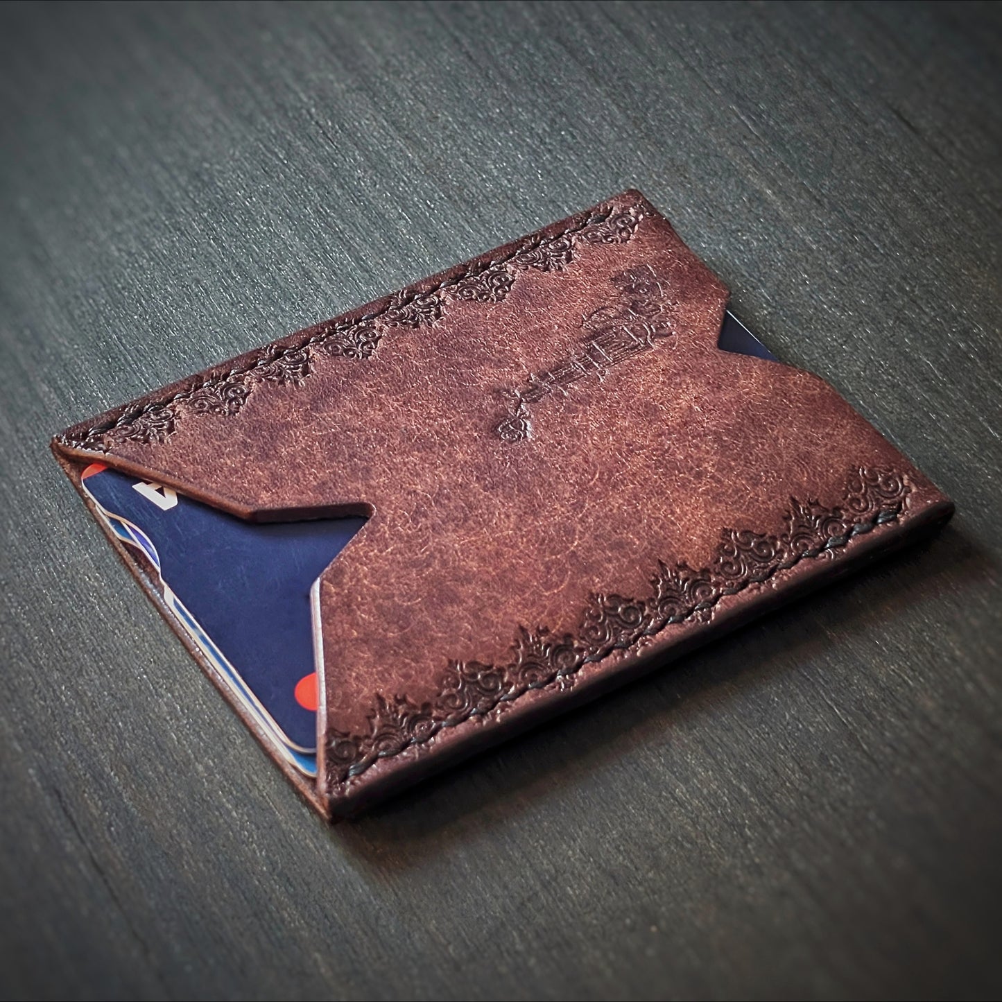 Angled view of El Rey Leather's Deadbeat minimalist cardholder in tobacco with cards, showing the gothic border.