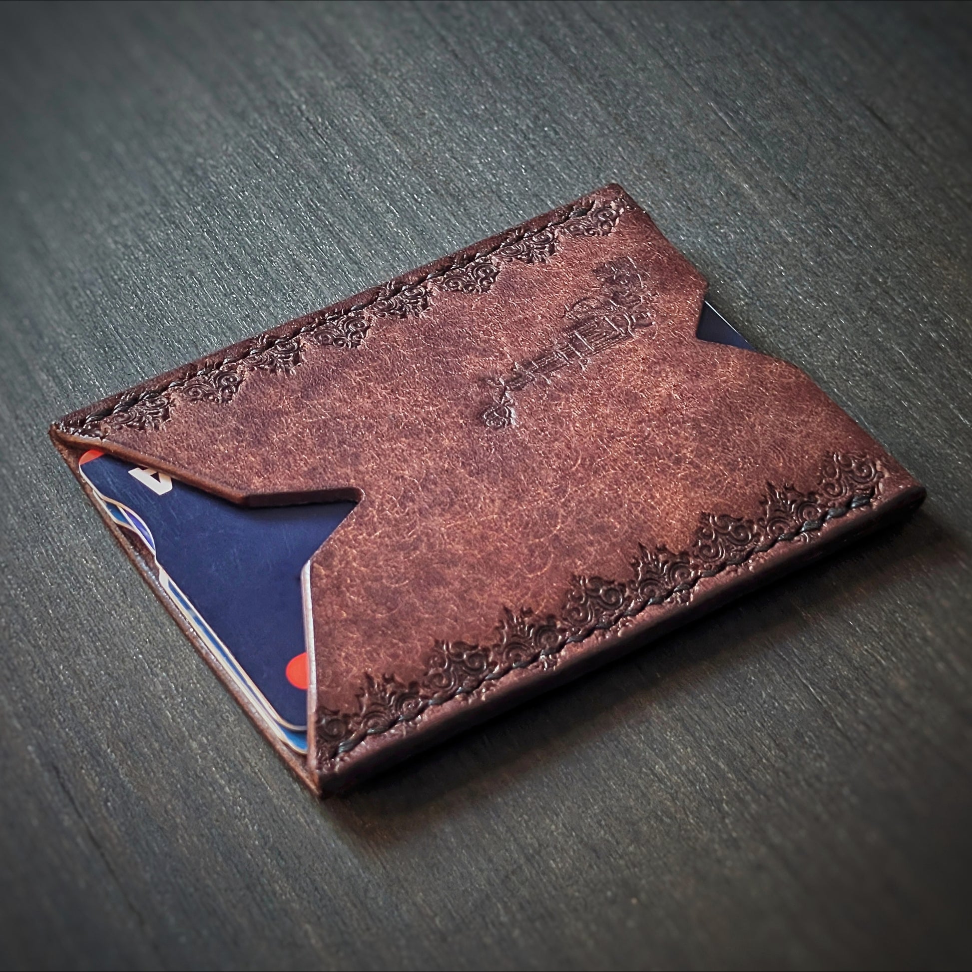 Angled view of El Rey Leather's Deadbeat minimalist cardholder in tobacco with cards, showing the gothic border.